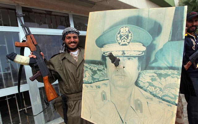 الصورة: أحد الثوار يحمل صورة للقذافي وعليها خنجراً