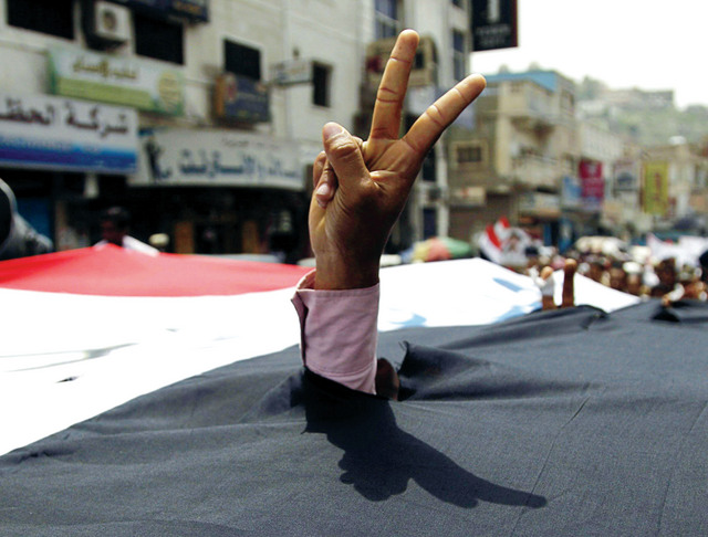 "متظاهر مناوئ للرئيس علي صالح يرفع شارة النصر مخترقاً علماً كبيراً كتب عليه: «الشعب يريد مجلساً انتقالياً» (رويترز)"