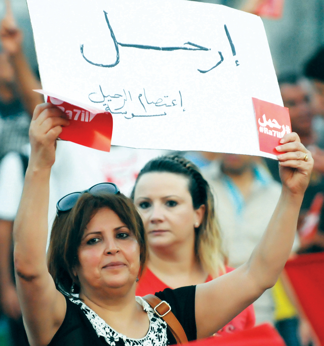 "متظاهرة تونسية تحمل لافتة تدعو فيها النظام للرحيل في ولاية سوسة بتونس.   أ.ف.ب"