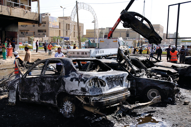 "رجال أمن وعمال إنقاذ يرفعون سيارة دمرها احد تفجيرات بغداد «أ.ب»"