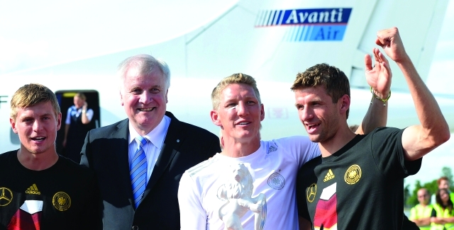"German national football team players Toni Kroos (L), Thomas Mueller (R) and Bastian Schweinsteiger (2nd R) pose with Bavaria's State Premier Horst Seehofer (2nd L) after arriving at the airport in Munich, southern Germany, on July 15, 2014. After attending a victory parade in Berlin, the Bayern Munich players of the national team and other players took a plane to Munich, where they were expected by thousands of football fans celebrating the 2014 FIFA Football World Cup title. AFP PHOTO / CHRISTOF STACHE"