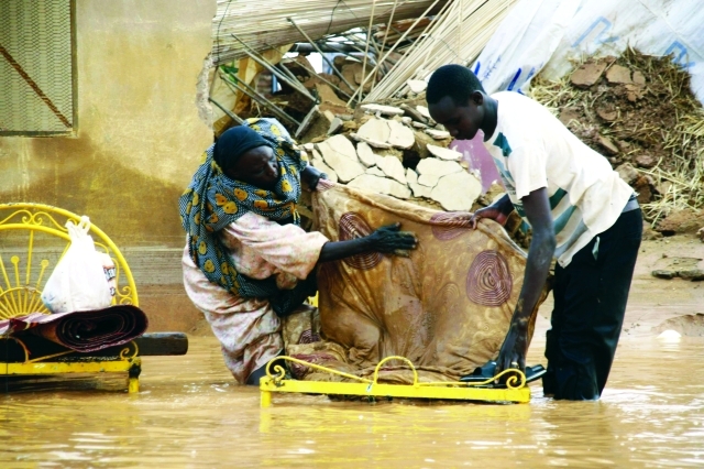 "سوداني يساعد امرأة مسنة على نقل أمتعتها وسط مياه الفيضانات في الخرطومرويترز"