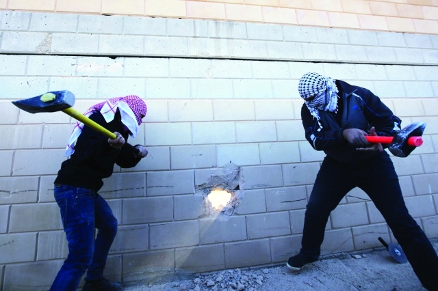 "شابان فلسطينيان يعملان على إحداث فتحة في الجدار الفاصل بين رام الله والقدس المحتلتين"