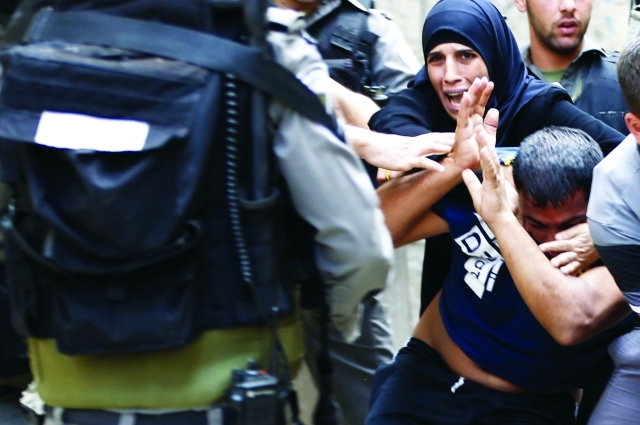 "■  فلسطينية تحاول إنقاذ أحد الشبان من أيدي جنود الاحتلال  |  أ.ف.ب"
