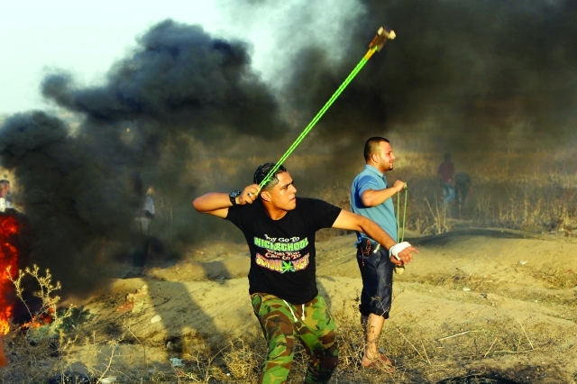"■ متظاهر فلسطيني يقذف حجراً باتجاه جنود الاحتلال خلال اشتباكات قرب السياج الحدودي بين إسرائيل وقطاع غزة | أ.ف.ب"