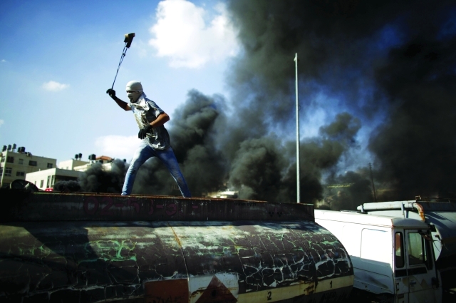 "■ فلسطيني يوجّه حجارته إلى جنود الاحتلال قرب إحدى المستوطنات الإسرائيلية | رويترز"