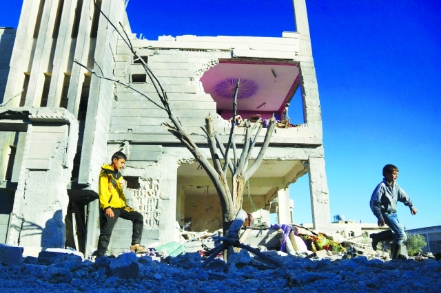"■ طفلان يسيران بقرب مبنى متضرر جراء الغارات في درعا | رويترز"