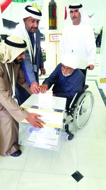 "■ علي الطنيجي يساعد مسناً في عملية التصويت في مركز المدام"