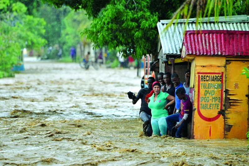 "TOPSHOT - People try to cross the overflowing La Rouyonne river in the commune of Leogane, south of Port-au-Prince, October 5, 2016. Haiti and the eastern tip of Cuba -- blasted by Matthew on October 4, 2016 -- began the messy and probably grim task of assessing the storm's toll. Matthew hit them as a Category Four hurricane but has since been downgraded to three, on a scale of five, by the US National Hurricane Center. / AFP / HECTOR RETAMAL"
