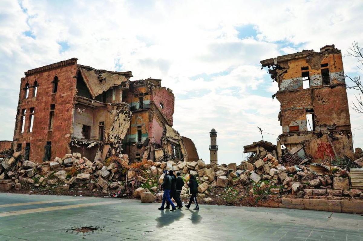 سوريون يسيرون أمام أحد المباني المدمرة في حلب قرب القلعة التاريخية للمدينة