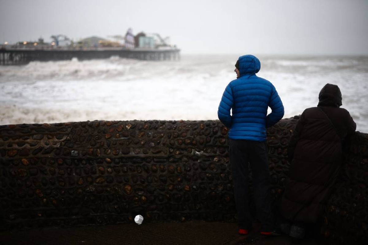 شخصان ينظران إلى الأمواج المتحطمة على الرصيف في برايتون جنوب إنجلترا 