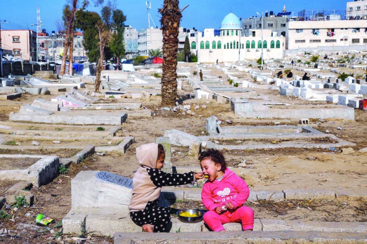 طفل يطعم صديقه بينما يجلسان في مقبرة في دير البلح