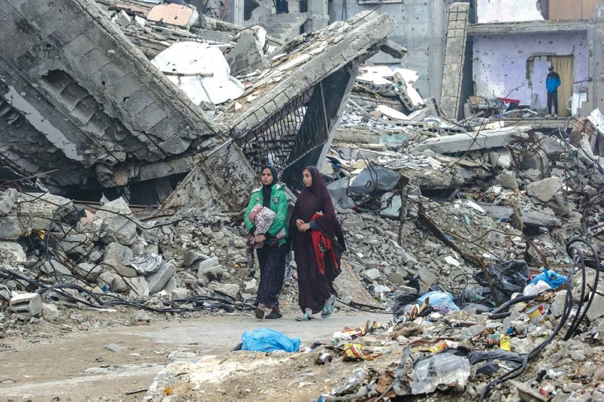 فلسطينيتان تسيران وسط الدمار بمخيم الشاطئ للاجئين في غزة