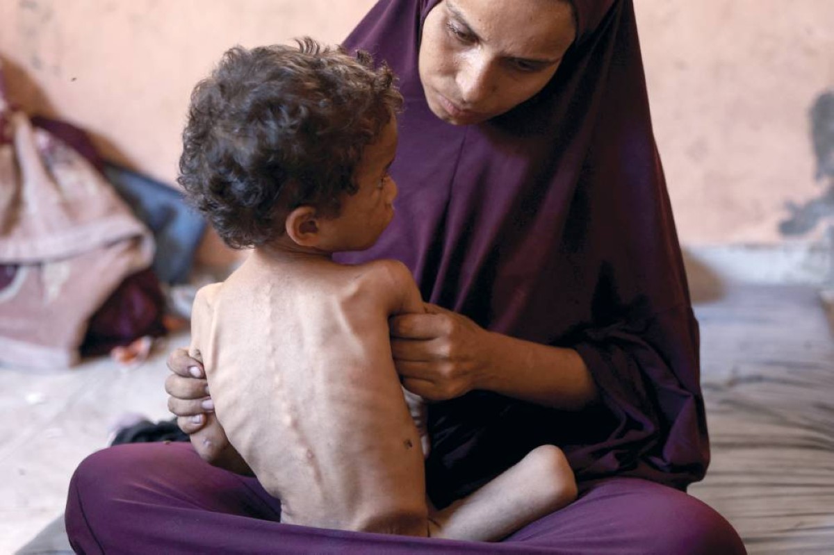 أم فلسطينية تجلس مع طفلها البالغ عامين ويعاني من الجوع في مخيم الشاطئ