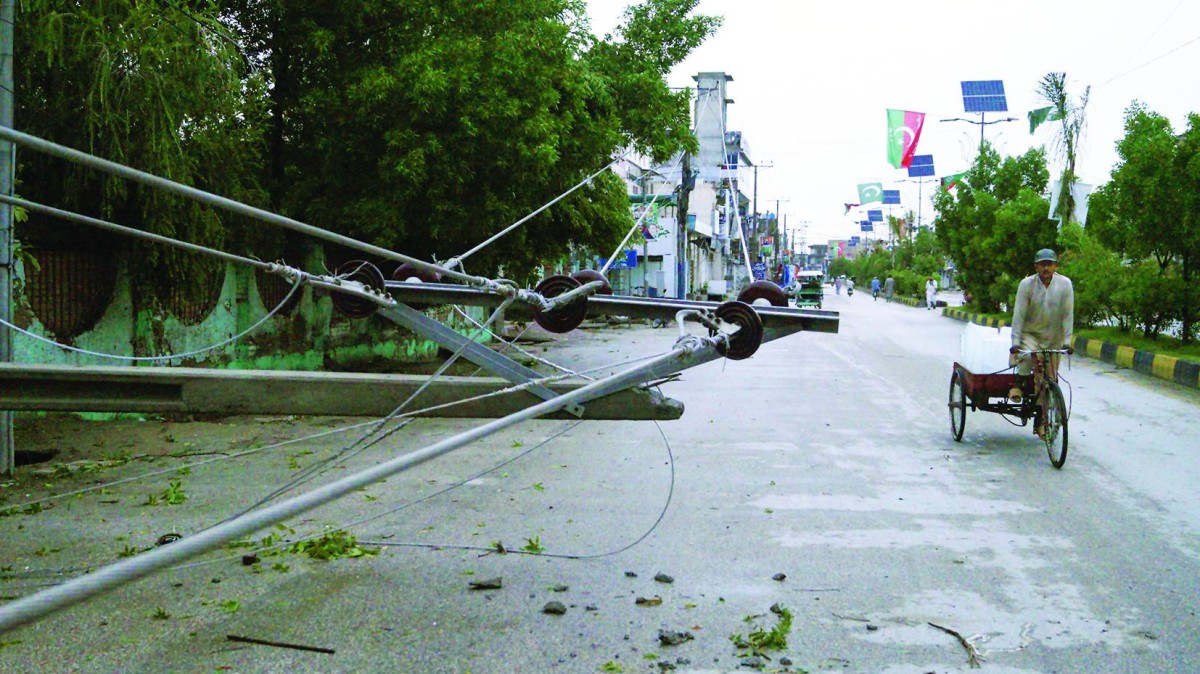 باكستاني يمر بجانب عمود كهرباء أسقطته الرياح بمنطقة ديرا إسماعيل خان