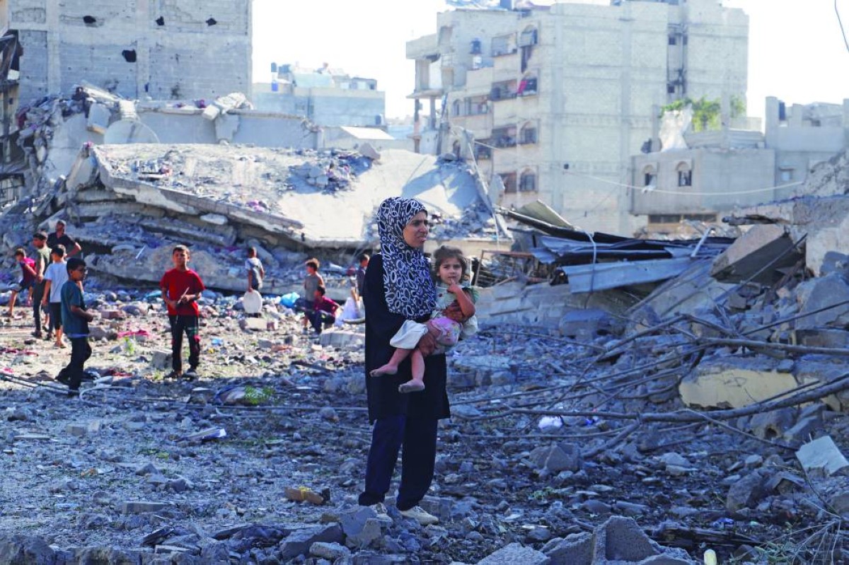 فلسطينية تحمل طفلة بين الدمار بعد غارة إسرائيلية على منزل بغزة