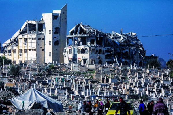 فلسطينيون يسيرون بالقرب من المقبرة القديمة المدمرة في مدينة غزة