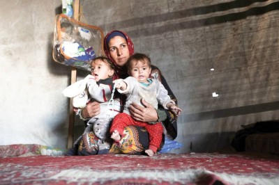 فلسطينية نازحة تحمل طفليها داخل خيمة بينما تكافح العائلات من أجل التدفئة خلال فصل الشتاء في خان يونس