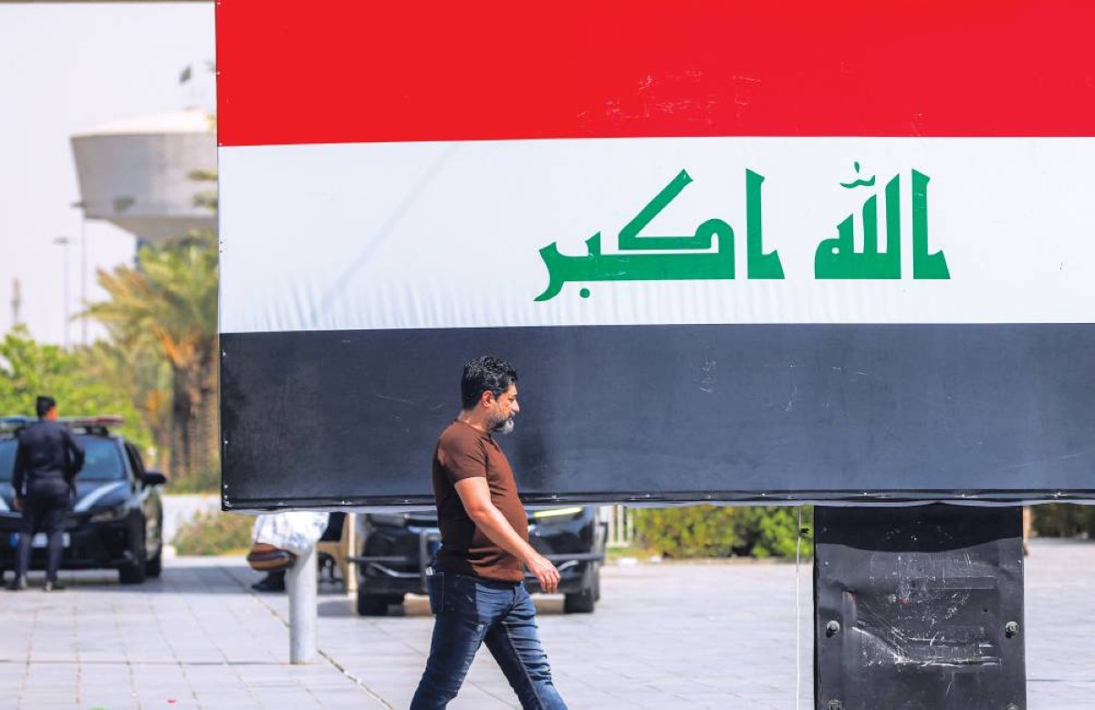 رجل يسير أمام لوحة إعلانية تحمل العلم العراقي في بغداد