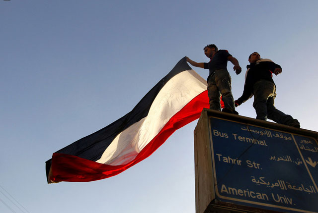 الصورة: متظاهرون يقفون فوق لائحة للإعلانات حاملين العلم المصري