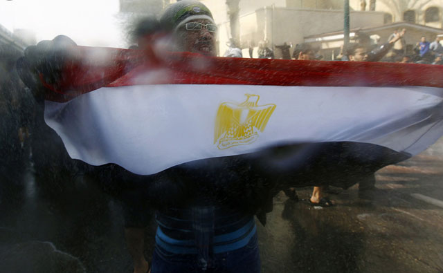 الصورة: متظاهر يحمل العلم المصري ويقف أمام المدافع خلال الإشتباكات في القاهرة