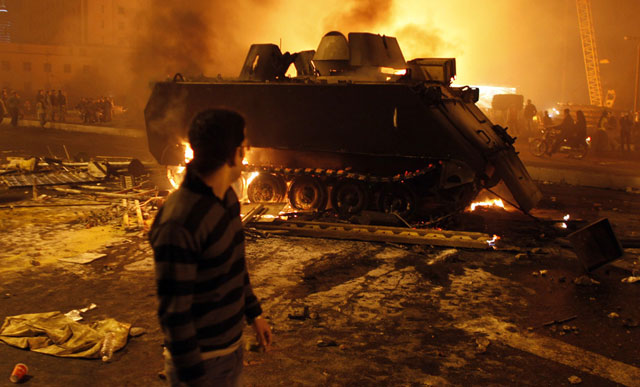 الصورة: متظاهر ينظر إلى دبابة الجيش المحترقة