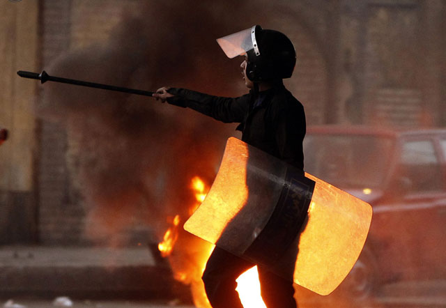 الصورة: أحد رجال شرطة مكافحة الشغب أمام إطارات مشتعلة وضعت لتشكل حاجزا خلال الاشتباكات مع المحتجين في القاهرة، 26 يناير 2011