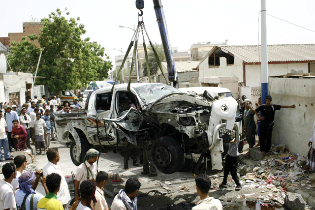 الصورة : يمنيون أمام سيارة دمرها التفجير الانتحاري
