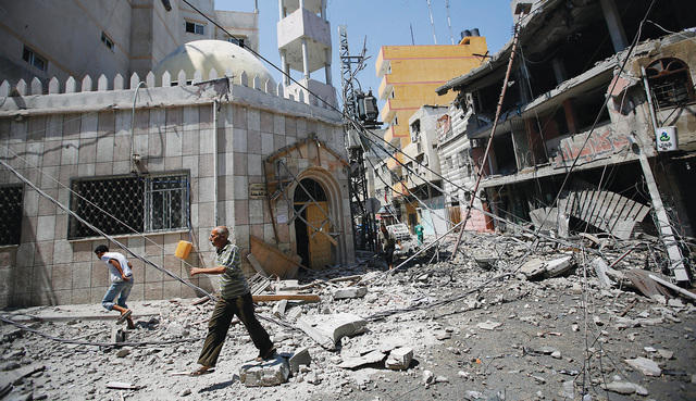 الصورة : فلسطينيان وسط الدمار الذي أحدثه القصف الإسرائيلي على منازل في مدينة غزة إي بي أيه