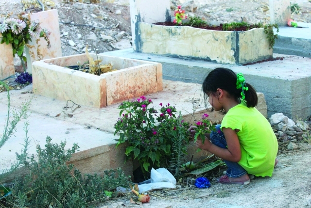 الصورة : طفلة سورية تضع الزهور على قبر قريب لها في مقبرة الشهداء في معرة النعمان 	رويترز