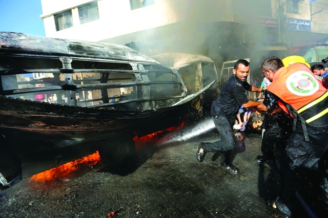 الصورة : فلسطينيون يحاولون إخماد النيران في حافلة بعد الغارات الجوية الإسرائيلية وسط غزة          اي.بي.اي