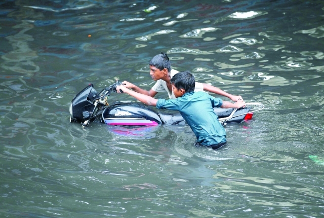 الصورة : طفلان هنديان يجهدان لاجتياز مياه الفيضانات بدراجة نارية معطلة في أحمد أباد رويترز