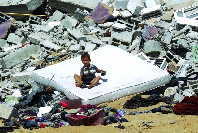 الصورة : طفل فلسطيني يجلس على فراش على أنقاض منزل أسرته في خان يونس الذي  دُمر بغارة جوية  أ.ف.ب