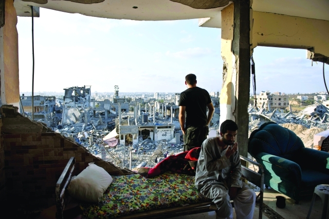 الصورة : شابان يجلسان على أنقاض منزلهما في غزة   وقربهما حي مدمر       			       	                       أ.ف.ب