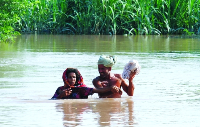 الصورة : باكستاني مع امرأة مسنة يخترقان مياه الفيضان الذي غمر أجزاء واسعة من شرق البنجاب    	 أ.ب