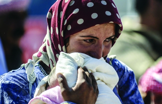 الصورة : نازحة كردية تذرف الدموع وهي تحمل طفلها الرضيع لدى اجتيازها الحدود إلى تركيا    								   أ.ف.ب