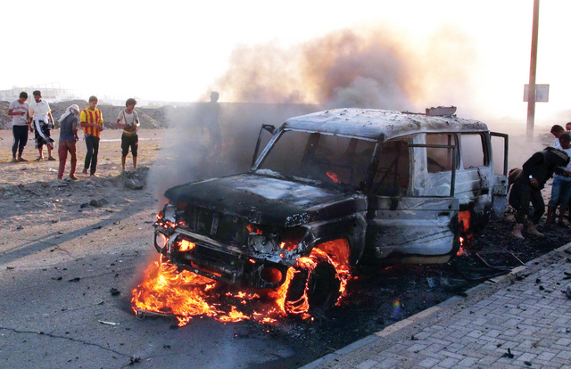 الصورة : يمنيون بجانب سيارة عسكرية للحوثيين تم تدميرها في الضربات  - إي.بي.إيه