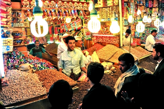 الصورة : epa02884085 A Yemeni vendor (C) displays a wide range of confectionery for sale during preparations for the Eid Al-Fitr at a traditional market in the Old City of Sana’a, Yemen, on 27 August 2011. Muslims throughout the world buy clothes and other popular items to prepare for the Eid-al-fitr, the festivities marking the end of the holy fasting month of Ramadan.  EPA/YAHYA ARHAB