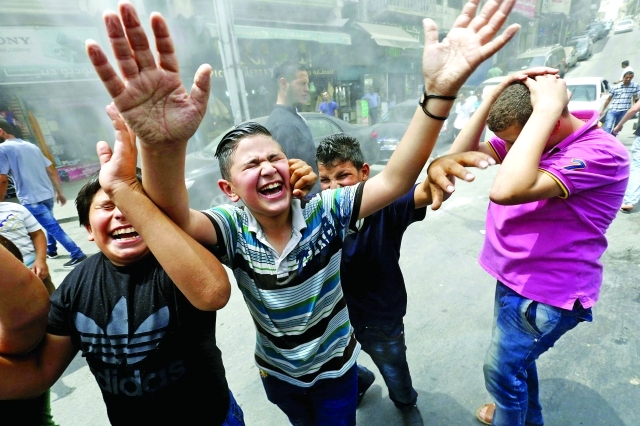 الصورة : ■ أطفال يتفاعلون مع  موظفي أمانة عمّان الكبرى أثناء رشهم برذاذ المياه من أجل تخفيف الحرارة  |   رويترز