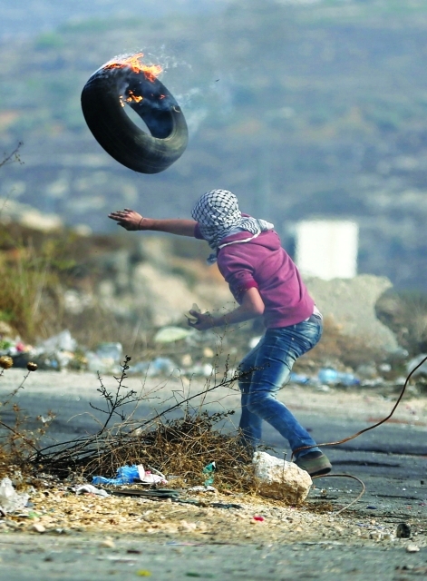 الصورة : ■ شاب فلسطيني يرمي إطاراً مشتعلاً باتجاه جيش الاحتلال قرب رام الله   |  رويترز