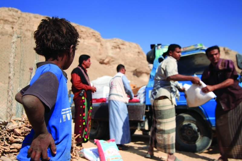 الصورة : طفل يشاهد مشرف التوزيع أثناء قيامه بمهامه في منطقة ساه بحضرموت