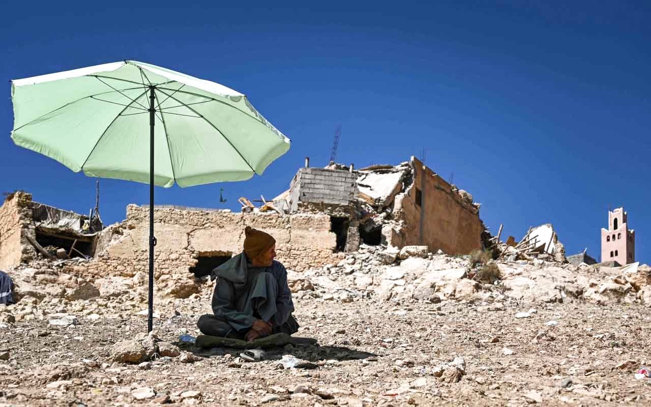 الصورة : أحد السكان يجلس بالقرب من مبانٍ مهدمة بسبب الزلزال في قرية بإقليم الحوز | أ.ف.ب