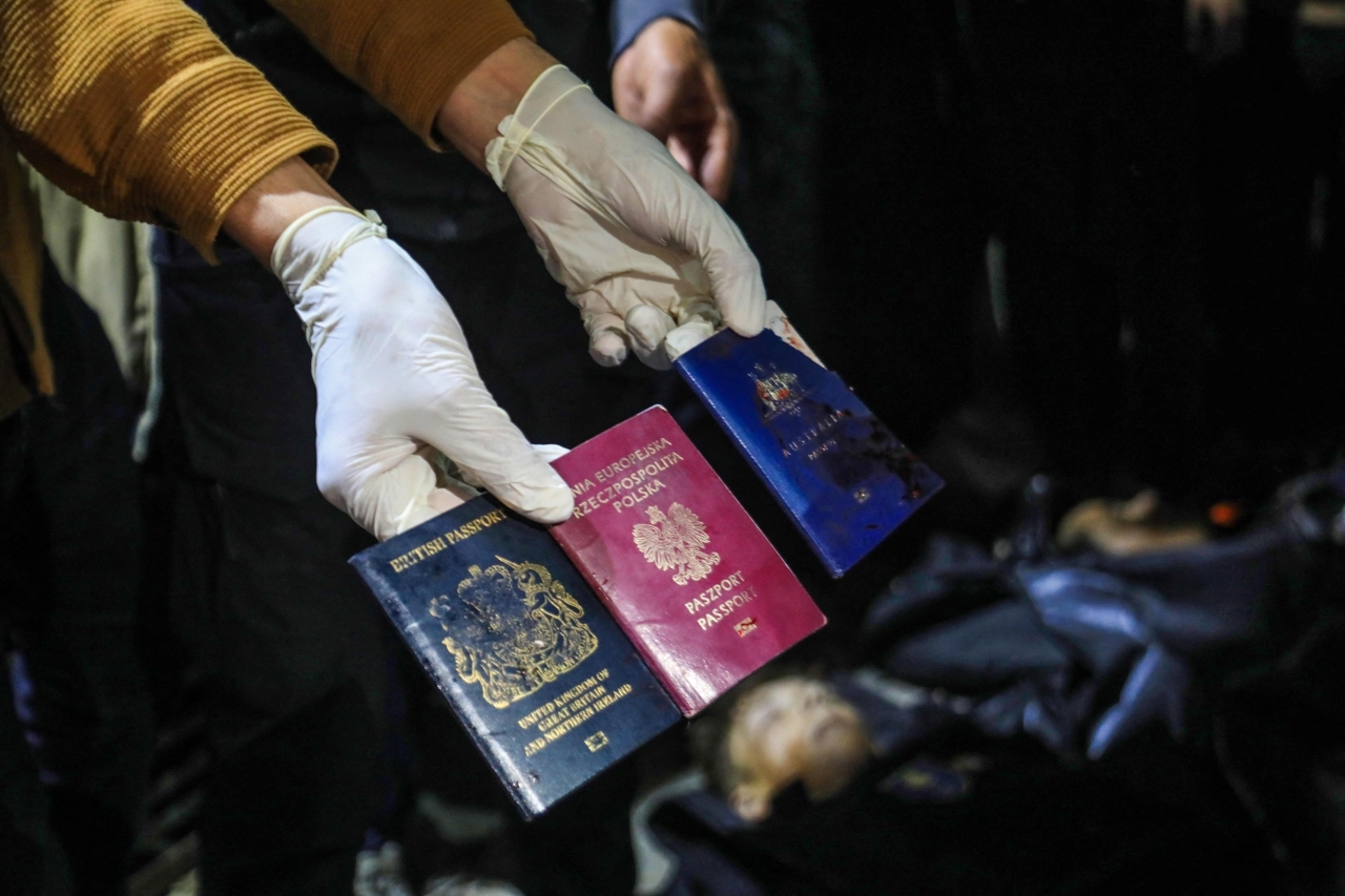الصورة : رجل يعرض جوازات السفر البريطانية والبولندية والأسترالية بجوار جثث الضحايا بمستشفى الأقصى في دير البلح | أ.ف.ب